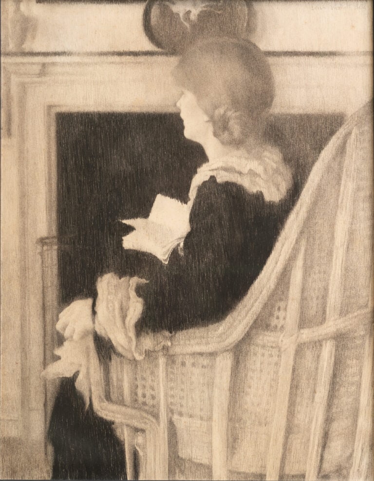 Woman sitting in armchair by fireplace with back turned to viewer. Book in right hand.