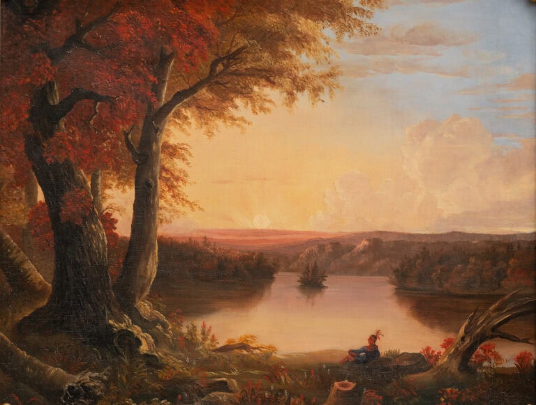 native american sitting lakeside under autumn tree at sunset
