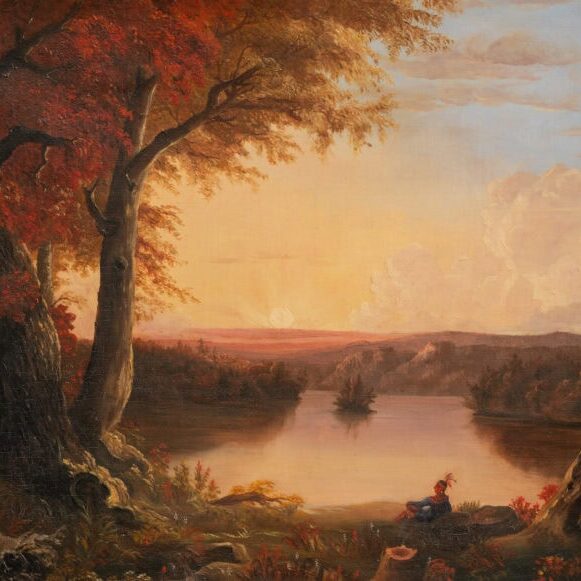native american sitting lakeside under autumn tree at sunset